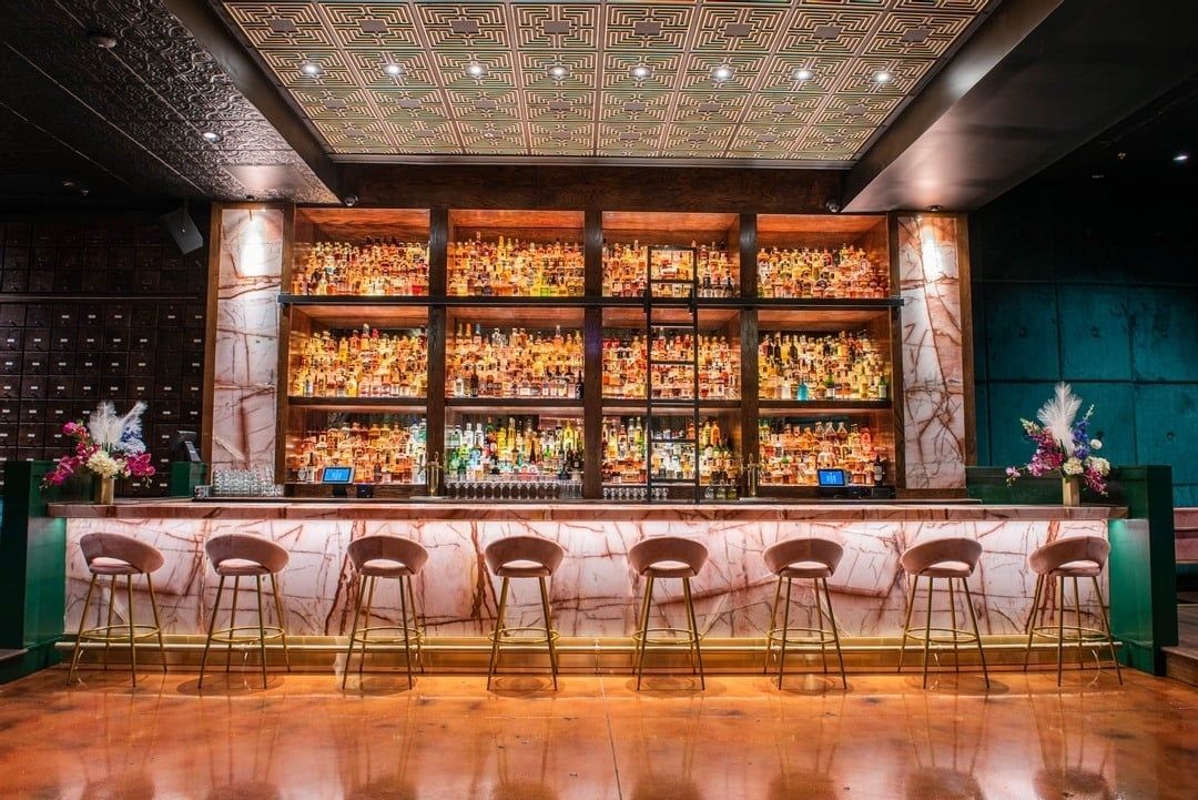 An image of a front-facing bar with empty bar stools. The bar is filled with various drinks.