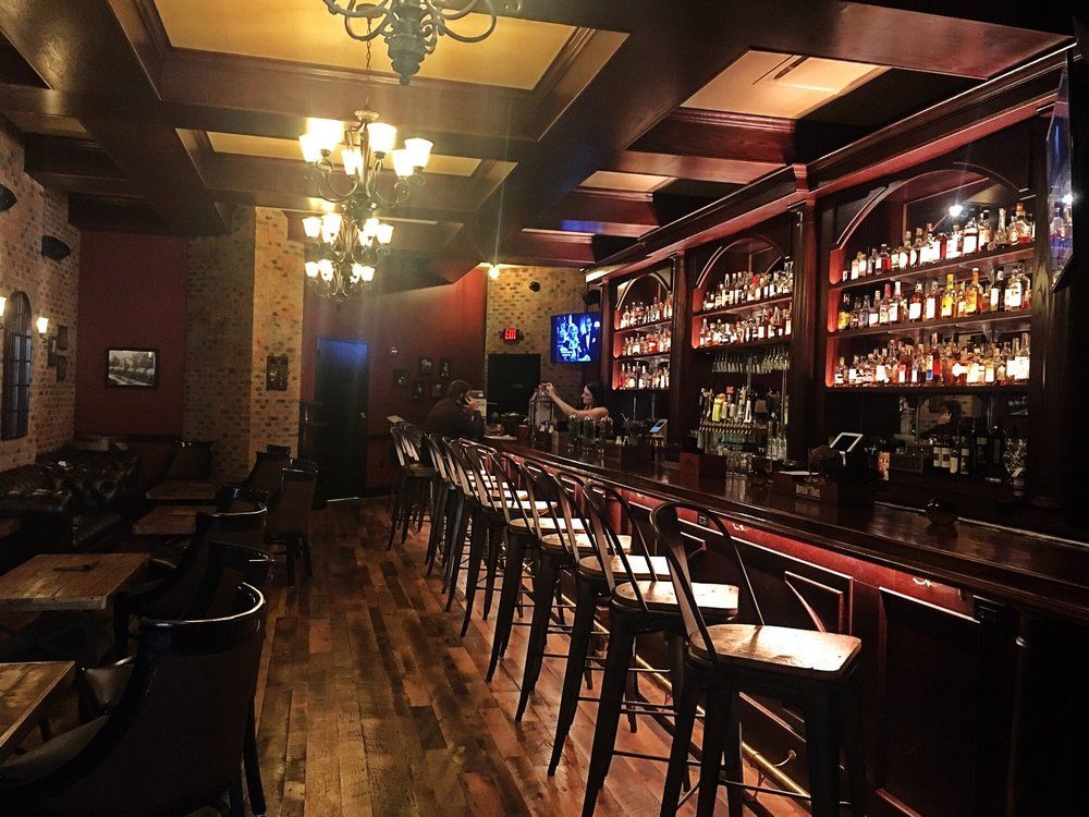 Wiseguy Lounge’s bar with lights above empty chairs and shelves filled with bottled liquor behind the counter