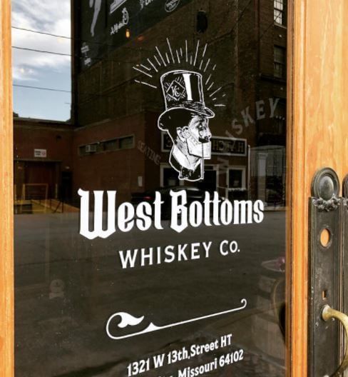 &nbsp;An image of West Bottoms Whiskey Co.’s glass door with the logo of the distillery on it