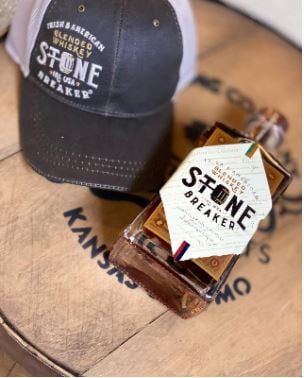 A bottle of whiskey on a whiskey barrel with a black and white hat